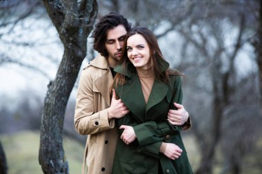 Genç ve şık bir çiftin güzel şehvetli portresi. Parkta yağmurluk giymiş güzel esmer bir çiftin resmi. Mutlu aile