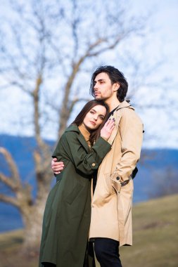 Genç ve şık bir çiftin güzel şehvetli portresi. Parkta yağmurluk giymiş güzel esmer bir çiftin resmi. Mutlu aile