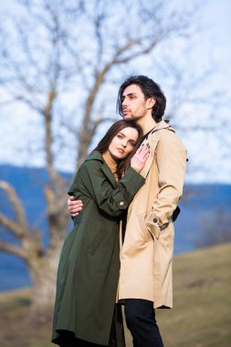 Genç ve şık bir çiftin güzel şehvetli portresi. Parkta yağmurluk giymiş güzel esmer bir çiftin resmi. Mutlu aile