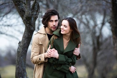 Genç ve şık bir çiftin güzel şehvetli portresi. Parkta yağmurluk giymiş güzel esmer bir çiftin resmi. Mutlu aile