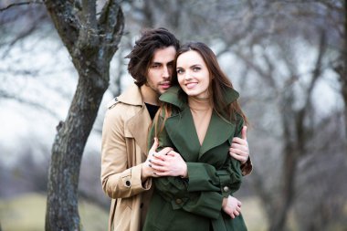 Genç ve şık bir çiftin güzel şehvetli portresi. Parkta yağmurluk giymiş güzel esmer bir çiftin resmi. Mutlu aile