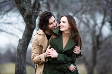 Genç ve şık bir çiftin güzel şehvetli portresi. Parkta yağmurluk giymiş güzel esmer bir çiftin resmi. Mutlu aile