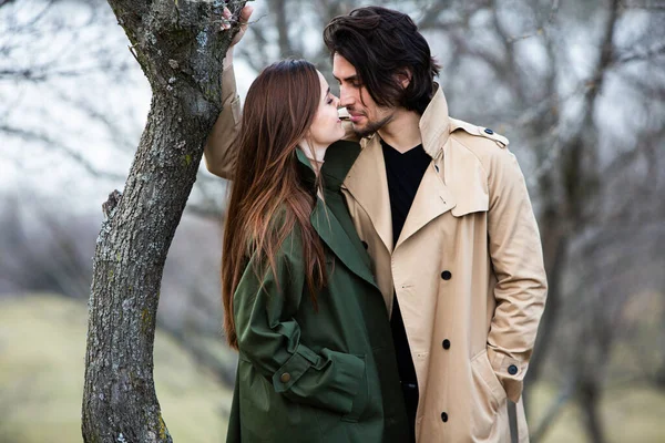 Genç ve şık bir çiftin güzel şehvetli portresi. Parkta yağmurluk giymiş güzel esmer bir çiftin resmi. Mutlu aile