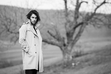 Soğuk havada yağmurluk giyen uzun saçlı güzel bir adamın görüntüsü. Bahar doğasında düşünen Avrupalı adam.