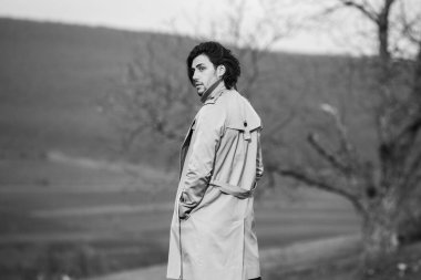 Soğuk havada yağmurluk giyen uzun saçlı güzel bir adamın görüntüsü. Bahar doğasında düşünen Avrupalı adam.