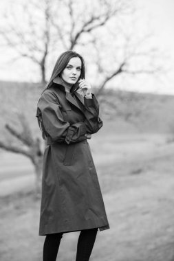 Soğuk havada yağmurluk giyen güzel bir kadın resmi. Bahar doğasında Düşünen Avrupalı kız.