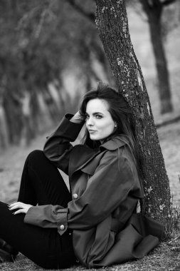 Soğuk havada yağmurluk giyen güzel bir kadın resmi. Bahar doğasında Düşünen Avrupalı kız.