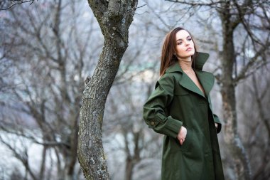 Soğuk havada yağmurluk giyen güzel bir kadın resmi. Bahar doğasında Düşünen Avrupalı kız.