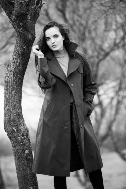 Soğuk havada yağmurluk giyen güzel bir kadın resmi. Bahar doğasında Düşünen Avrupalı kız.