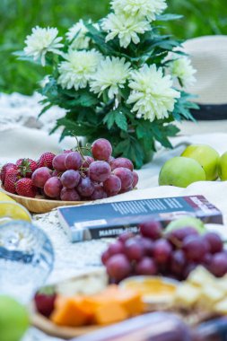 Outdoors picnic in a lush green park with a tasty croissant, fruits, donuts and wine on grass. Summer picnic on the blanket.