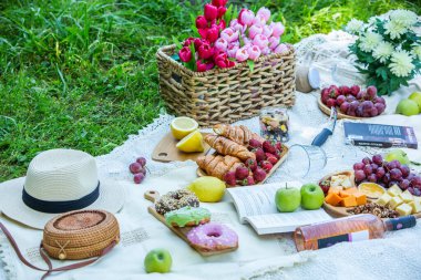Outdoors picnic in a lush green park with a tasty croissant, fruits, donuts and wine on grass. Summer picnic on the blanket.