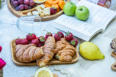 Outdoors picnic in a lush green park with a tasty croissant, fruits, donuts and wine on grass. Summer picnic on the blanket.