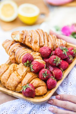Outdoors picnic in a lush green park with a tasty croissant, fruits, donuts and wine on grass. Summer picnic on the blanket.