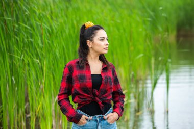 Esmer kız, nehirde lastik çizmelerle eğleniyor. Göldeki genç kadın hayatın tadını çıkar.