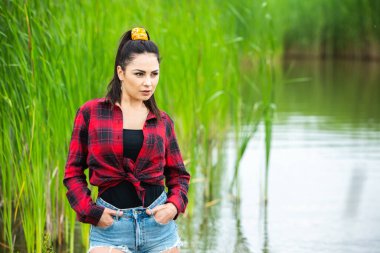 Esmer kız, nehirde lastik çizmelerle eğleniyor. Göldeki genç kadın hayatın tadını çıkar.