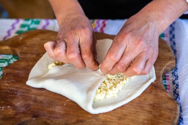 Geleneksel kıyafetlerle geleneksel Romen usulü kızarmış turta pişiren bir bayanın ellerindeki görüntü.