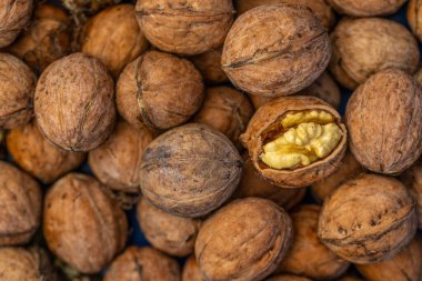walnuts and kernels captured in a rustic natural setting. Some nuts are cracked open, revealing the rich interior texture, while others remain whole on a dark wooden surface. 