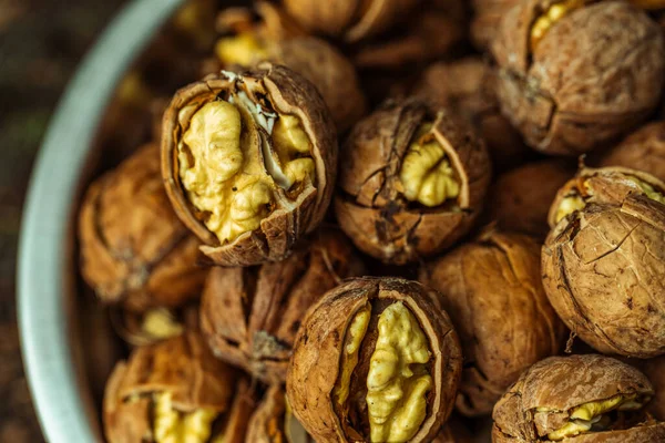 walnuts and kernels captured in a rustic natural setting. Some nuts are cracked open, revealing the rich interior texture, while others remain whole on a dark wooden surface. 