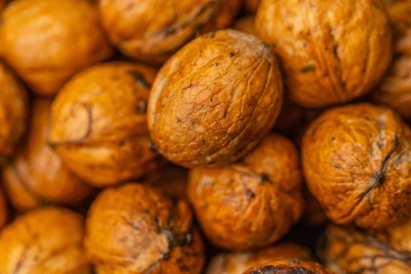 walnuts and kernels captured in a rustic natural setting. Some nuts are cracked open, revealing the rich interior texture, while others remain whole on a dark wooden surface. 