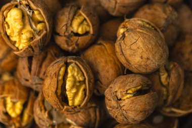 walnuts and kernels captured in a rustic natural setting. Some nuts are cracked open, revealing the rich interior texture, while others remain whole on a dark wooden surface. 