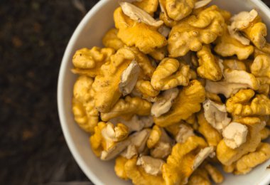 walnuts and kernels captured in a rustic natural setting. Some nuts are cracked open, revealing the rich interior texture, while others remain whole on a dark wooden surface. 