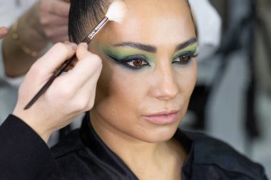 Zarif gözleri, canlı sanatsal makyajı ve fütüristik saç tasarımı olan zarif bir kadının yakın plan portresi. Renkli, yaratıcı makyajlı, desenli saç stili ve dramatik ışıklandırmalı genç bir kadının moda güzelliği.