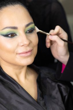 Zarif gözleri, canlı sanatsal makyajı ve fütüristik saç tasarımı olan zarif bir kadının yakın plan portresi. Renkli, yaratıcı makyajlı, desenli saç stili ve dramatik ışıklandırmalı genç bir kadının moda güzelliği.