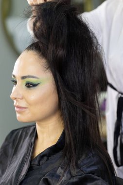 Zarif gözleri, canlı sanatsal makyajı ve fütüristik saç tasarımı olan zarif bir kadının yakın plan portresi. Renkli, yaratıcı makyajlı, desenli saç stili ve dramatik ışıklandırmalı genç bir kadının moda güzelliği.