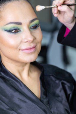 Zarif gözleri, canlı sanatsal makyajı ve fütüristik saç tasarımı olan zarif bir kadının yakın plan portresi. Renkli, yaratıcı makyajlı, desenli saç stili ve dramatik ışıklandırmalı genç bir kadının moda güzelliği.