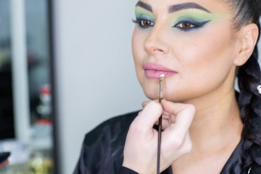 Zarif gözleri, canlı sanatsal makyajı ve fütüristik saç tasarımı olan zarif bir kadının yakın plan portresi. Renkli, yaratıcı makyajlı, desenli saç stili ve dramatik ışıklandırmalı genç bir kadının moda güzelliği.