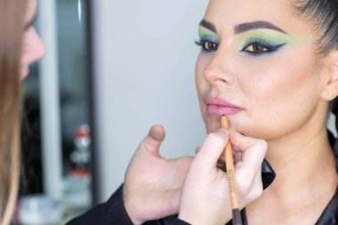 Zarif gözleri, canlı sanatsal makyajı ve fütüristik saç tasarımı olan zarif bir kadının yakın plan portresi. Renkli, yaratıcı makyajlı, desenli saç stili ve dramatik ışıklandırmalı genç bir kadının moda güzelliği.