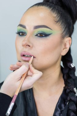 Zarif gözleri, canlı sanatsal makyajı ve fütüristik saç tasarımı olan zarif bir kadının yakın plan portresi. Renkli, yaratıcı makyajlı, desenli saç stili ve dramatik ışıklandırmalı genç bir kadının moda güzelliği.