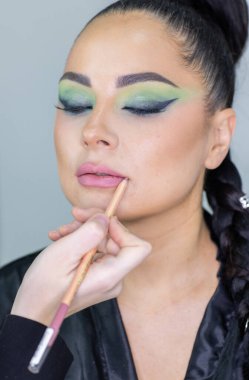 Zarif gözleri, canlı sanatsal makyajı ve fütüristik saç tasarımı olan zarif bir kadının yakın plan portresi. Renkli, yaratıcı makyajlı, desenli saç stili ve dramatik ışıklandırmalı genç bir kadının moda güzelliği.