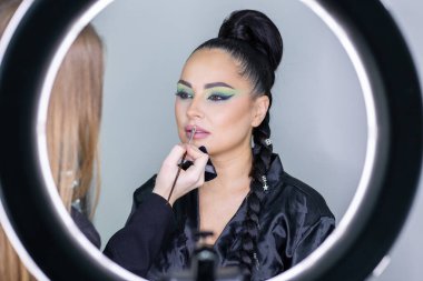 Zarif gözleri, canlı sanatsal makyajı ve fütüristik saç tasarımı olan zarif bir kadının yakın plan portresi. Renkli, yaratıcı makyajlı, desenli saç stili ve dramatik ışıklandırmalı genç bir kadının moda güzelliği.