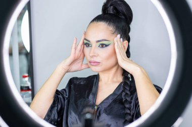 Zarif gözleri, canlı sanatsal makyajı ve fütüristik saç tasarımı olan zarif bir kadının yakın plan portresi. Renkli, yaratıcı makyajlı, desenli saç stili ve dramatik ışıklandırmalı genç bir kadının moda güzelliği.