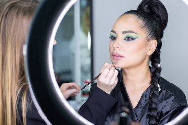 Zarif gözleri, canlı sanatsal makyajı ve fütüristik saç tasarımı olan zarif bir kadının yakın plan portresi. Renkli, yaratıcı makyajlı, desenli saç stili ve dramatik ışıklandırmalı genç bir kadının moda güzelliği.