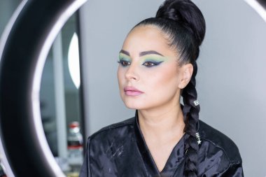 Zarif gözleri, canlı sanatsal makyajı ve fütüristik saç tasarımı olan zarif bir kadının yakın plan portresi. Renkli, yaratıcı makyajlı, desenli saç stili ve dramatik ışıklandırmalı genç bir kadının moda güzelliği.