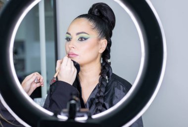 Zarif gözleri, canlı sanatsal makyajı ve fütüristik saç tasarımı olan zarif bir kadının yakın plan portresi. Renkli, yaratıcı makyajlı, desenli saç stili ve dramatik ışıklandırmalı genç bir kadının moda güzelliği.