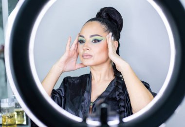 Zarif gözleri, canlı sanatsal makyajı ve fütüristik saç tasarımı olan zarif bir kadının yakın plan portresi. Renkli, yaratıcı makyajlı, desenli saç stili ve dramatik ışıklandırmalı genç bir kadının moda güzelliği.