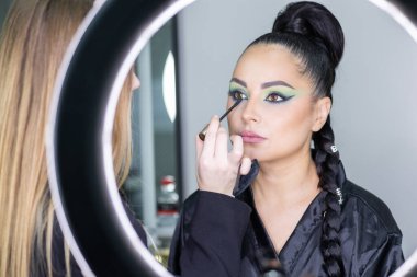 Zarif gözleri, canlı sanatsal makyajı ve fütüristik saç tasarımı olan zarif bir kadının yakın plan portresi. Renkli, yaratıcı makyajlı, desenli saç stili ve dramatik ışıklandırmalı genç bir kadının moda güzelliği.