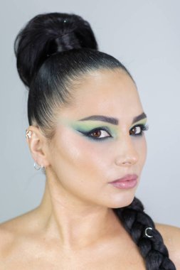 Zarif gözleri, canlı sanatsal makyajı ve fütüristik saç tasarımı olan zarif bir kadının yakın plan portresi. Renkli, yaratıcı makyajlı, desenli saç stili ve dramatik ışıklandırmalı genç bir kadının moda güzelliği.