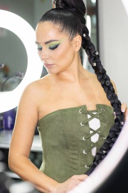 Zarif gözleri, canlı sanatsal makyajı ve fütüristik saç tasarımı olan zarif bir kadının yakın plan portresi. Renkli, yaratıcı makyajlı, desenli saç stili ve dramatik ışıklandırmalı genç bir kadının moda güzelliği.