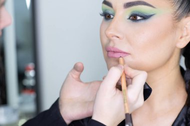 Beautiful European woman getting artistic makeup applied by a professional makeup artist in a modern beauty salon, beauty, glamour and elegance concept.