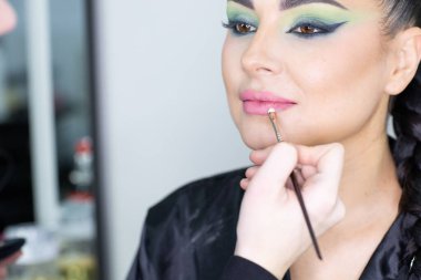 Beautiful European woman getting artistic makeup applied by a professional makeup artist in a modern beauty salon, beauty, glamour and elegance concept.