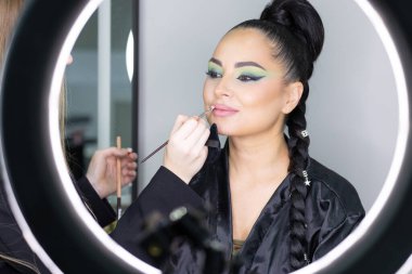 Beautiful European woman getting artistic makeup applied by a professional makeup artist in a modern beauty salon, beauty, glamour and elegance concept.
