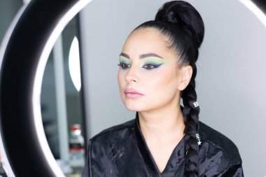 Beautiful European woman getting artistic makeup applied by a professional makeup artist in a modern beauty salon, beauty, glamour and elegance concept.