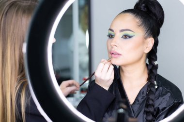 Beautiful European woman getting artistic makeup applied by a professional makeup artist in a modern beauty salon, beauty, glamour and elegance concept.