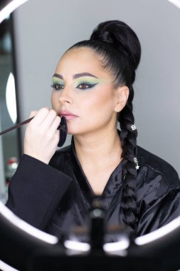 Beautiful European woman getting artistic makeup applied by a professional makeup artist in a modern beauty salon, beauty, glamour and elegance concept.