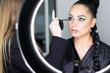 Beautiful European woman getting artistic makeup applied by a professional makeup artist in a modern beauty salon, beauty, glamour and elegance concept.