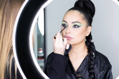 Beautiful European woman getting artistic makeup applied by a professional makeup artist in a modern beauty salon, beauty, glamour and elegance concept.